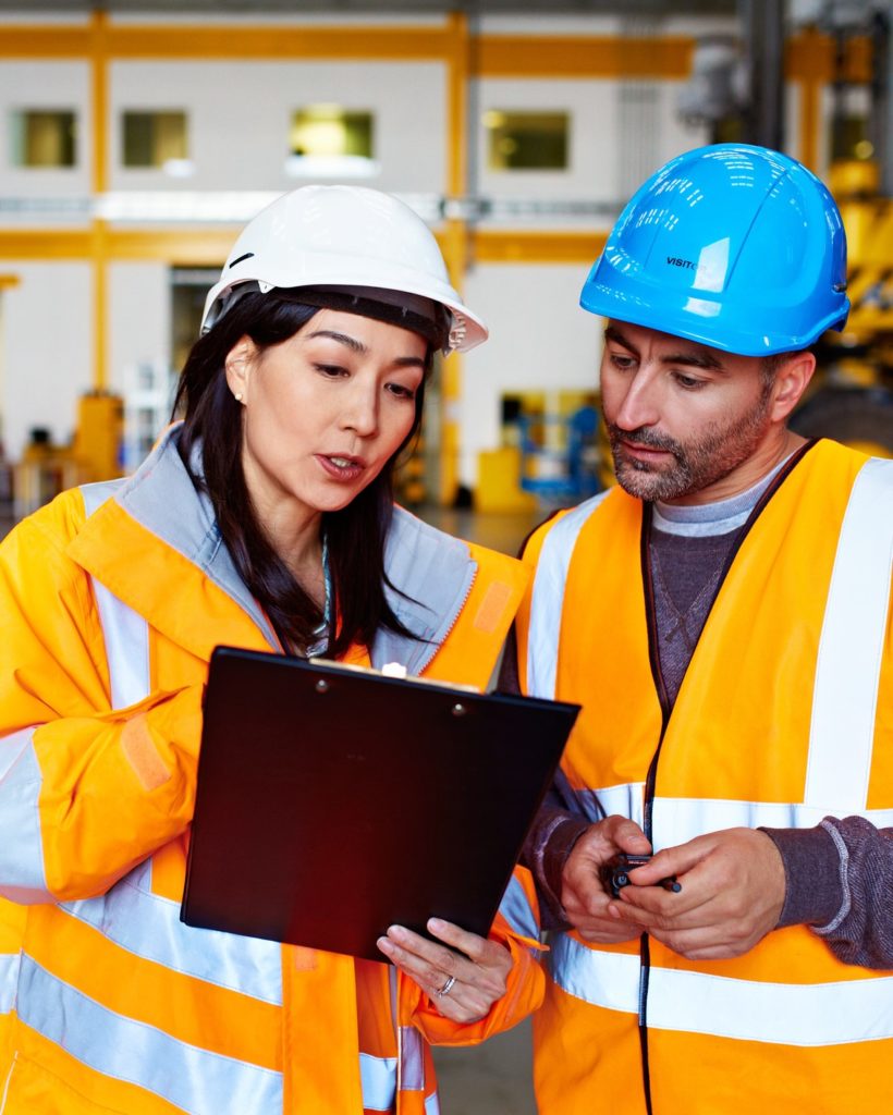 Shot of two warehouse workers talking together over a clipboard while standing inside of a large warehouse