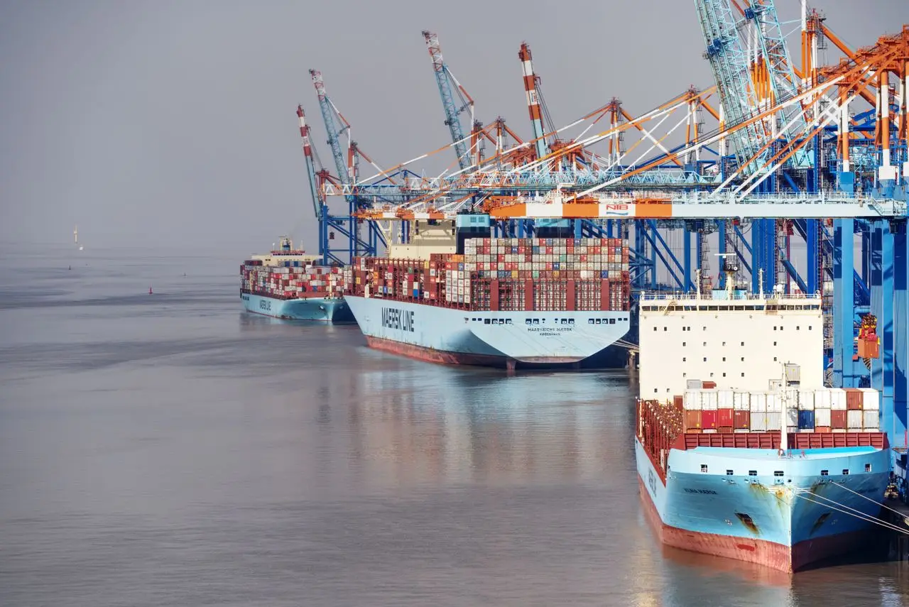 Container ships docked at a busy port with vibrant cranes and clear skies.